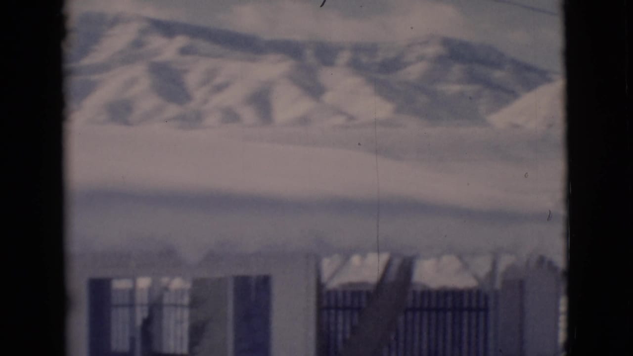 Snowy building, fence, hills, and dark vertical frame edge.