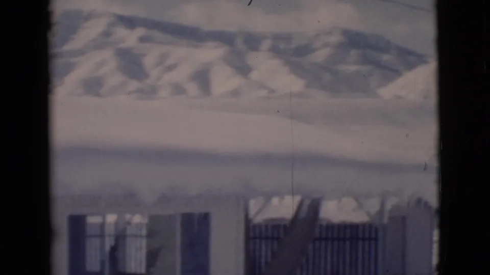 Snow-covered rural building and fence appear beneath distant hills in this 1966 Clarkdale home-movie frame.
