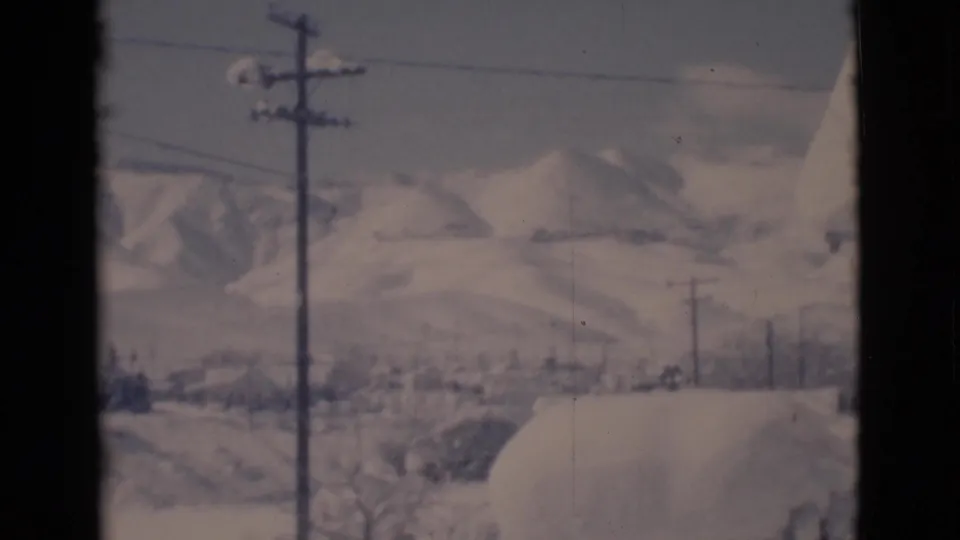 Snowy Clarkdale landscape with utility poles, power lines, distant hills, and a roof edge in a 1966 8mm frame.