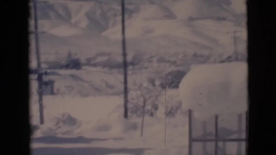 Clarkdale, Arizona 1966 frame with snowdrifts, utility poles, distant hills, shrubs, and a low structure partly obscured by snow.