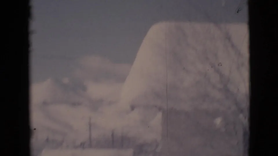 Soft 1966 8mm frame from Clarkdale showing a heavy snow cover over a roofline or mound, with faint winter trees beyond.