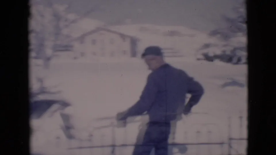 A man in a dark coat and cap continues shoveling snow beside an iron fence in the Clarkdale, Arizona winter yard.
