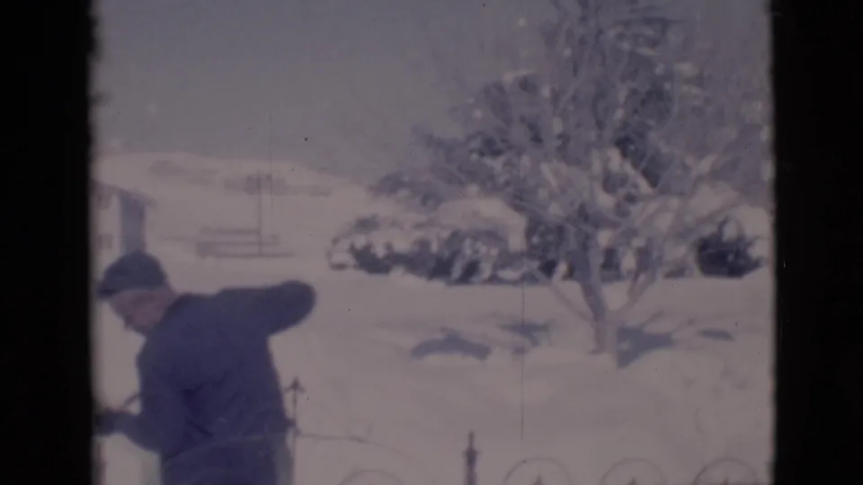 The man bends into the snow with his shovel as a bare tree, house, and snowbanks fill the 1966 Clarkdale winter scene.