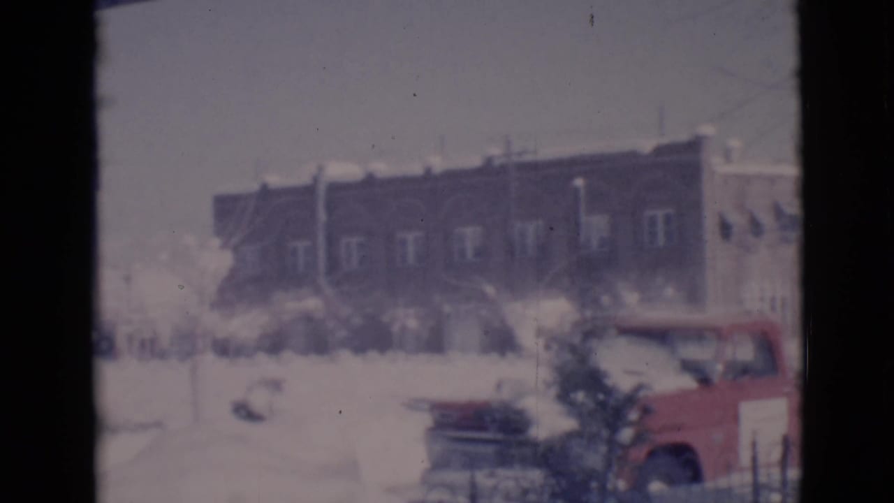 Snowy street with a red pickup truck near a brick building in the background.