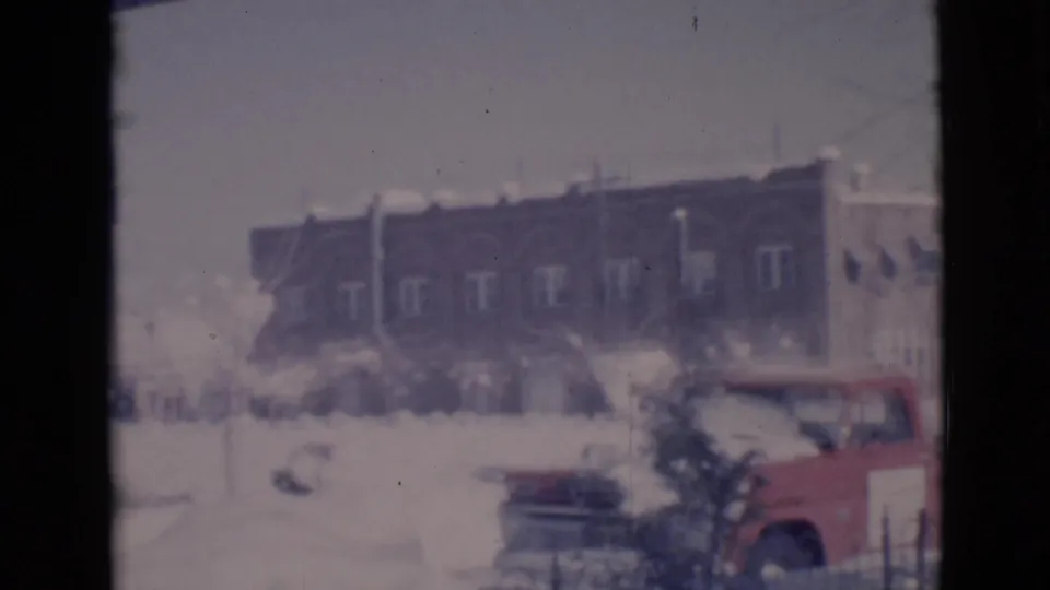 1966 Clarkdale, Arizona 8mm frame showing a red pickup beside a snow-covered street with a brick building beyond.