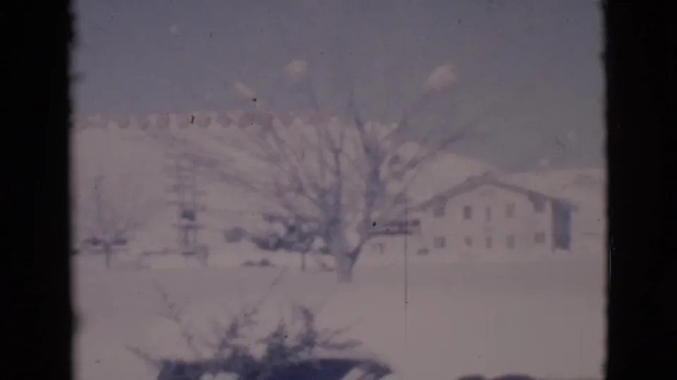 1966 Clarkdale, Arizona 8mm view of a snow-covered street, bare tree, utility pole, and pale building below a hillside.