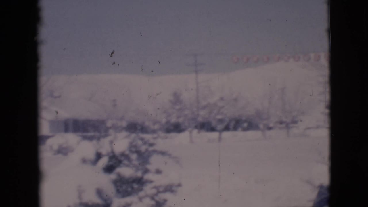 Snow-covered houses, trees, and utility poles in Clarkdale, Arizona, viewed through a window on 1966 8mm film.