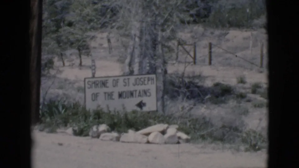 1966 Clarkdale, Arizona 8mm frame showing a roadside sign for Shrine of St Joseph of the Mountains with a left arrow.