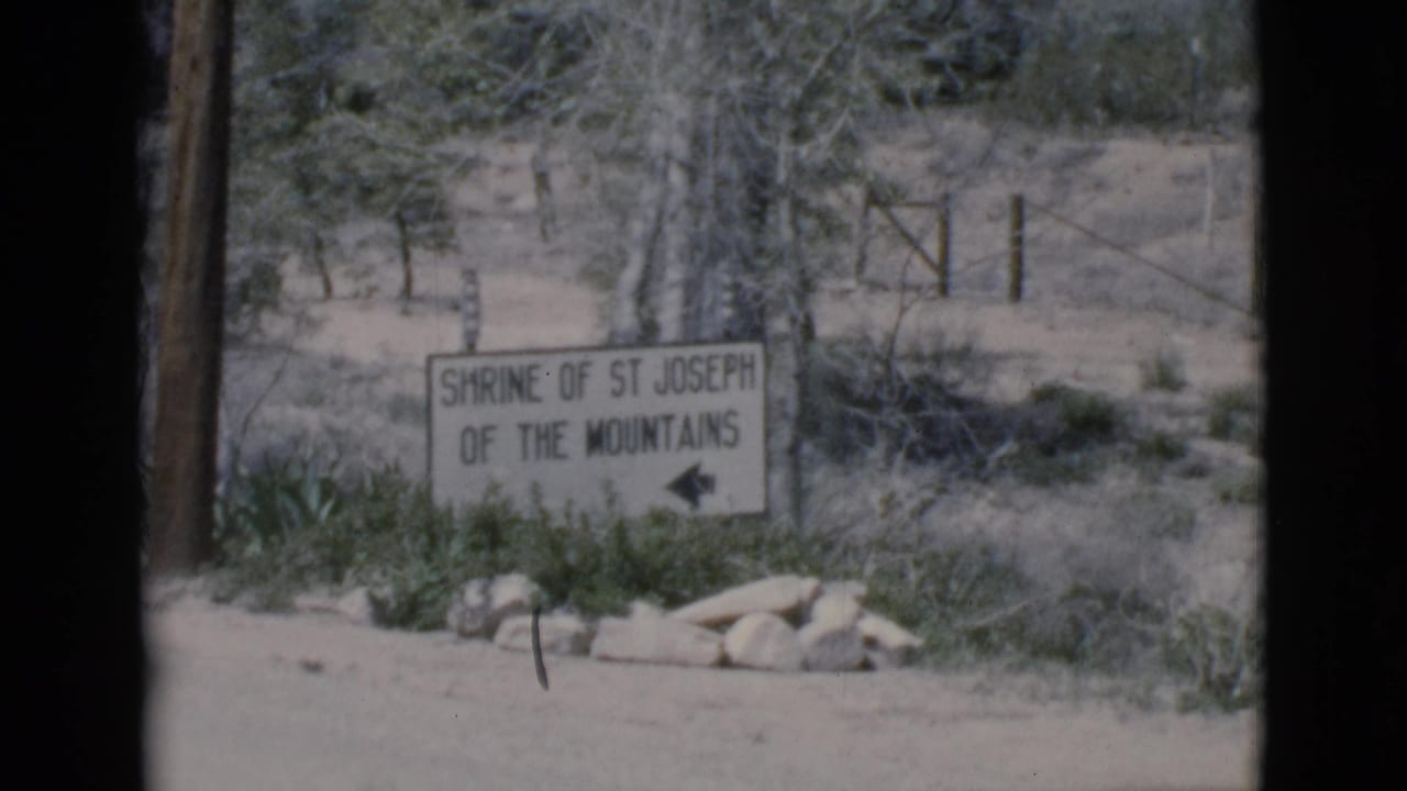 Roadside sign reading Shrine of St Joseph of the Mountains with an arrow beside desert scrub.