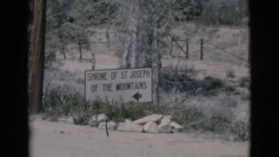 1966 Clarkdale, Arizona frame showing a Shrine of St Joseph of the Mountains direction sign near dry brush, rocks, and a utility pole.