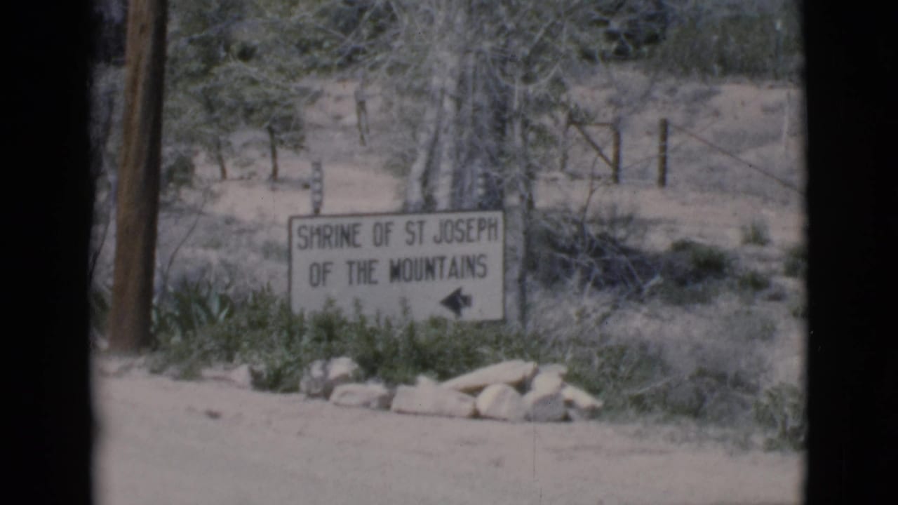 Shrine of St Joseph of the Mountains sign with arrow, trees, brush, and roadside ground.