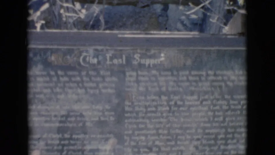 Close 8mm frame of a religious plaque titled The Last Supper, with small explanatory writing and shrine display material above.