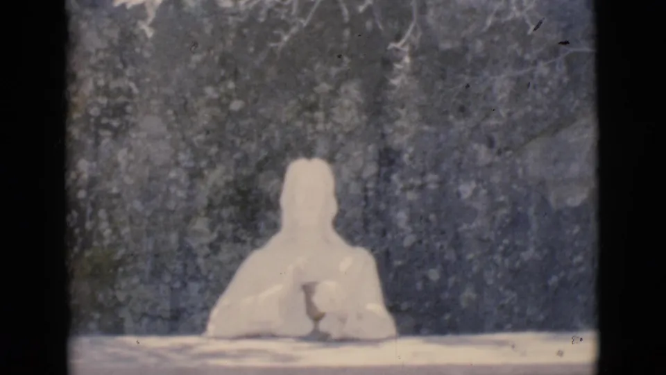 1966 Clarkdale 8mm frame showing a pale seated humanoid clay figure with clasped hands at a table before a dark textured background.
