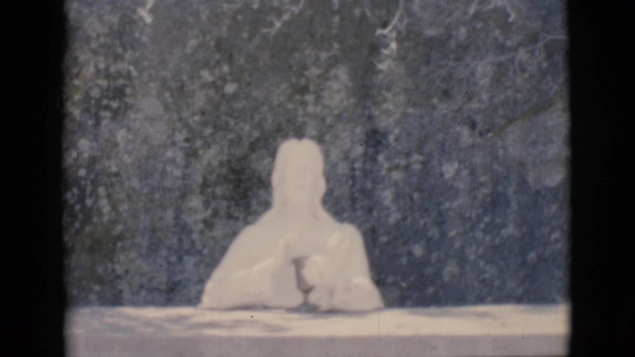 White seated humanoid figure remains centered behind a table with a dark mottled background.