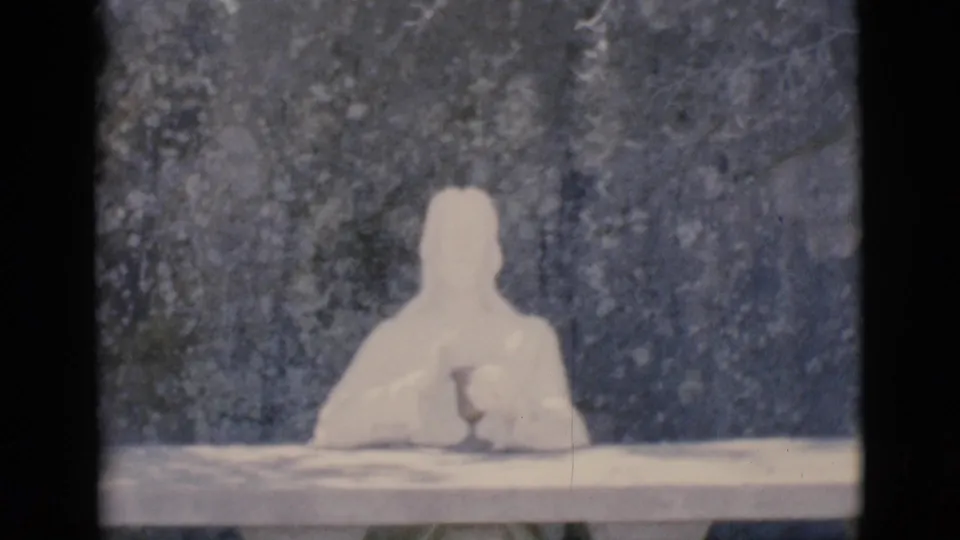1966 Clarkdale 8mm frame showing the same pale humanoid figure seated at a table, with soft focus and visible film grain.