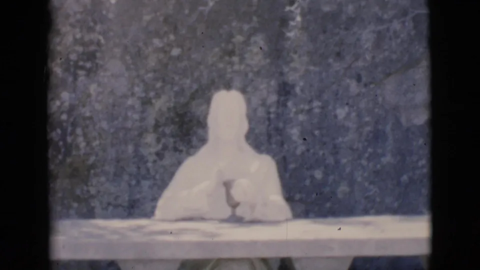 Final 1966 Clarkdale frame with the pale seated humanoid clay figure still posed at a table before a dark, branch-marked background.