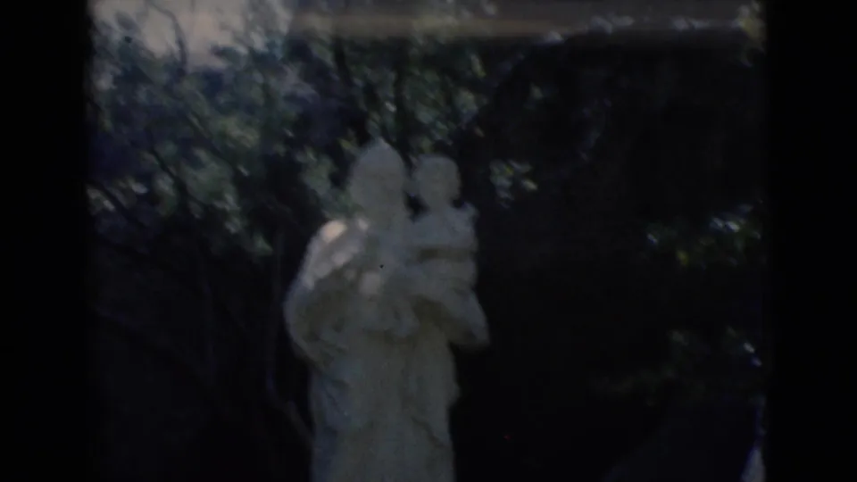 Outdoor 1966 Clarkdale frame showing a pale stone adult-and-child statue in deep shade among trees.