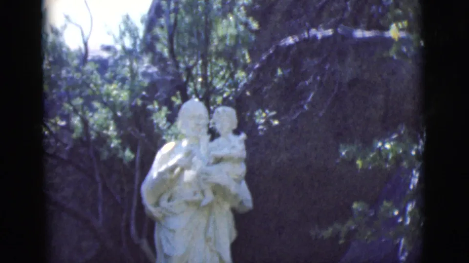 The final 8mm frame shows a white stone adult holding a child with a small cross, set before trees and rock.