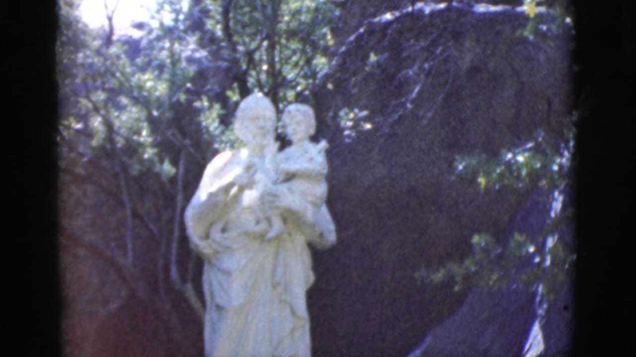 White outdoor statue framed by greenery with a dark rock background.