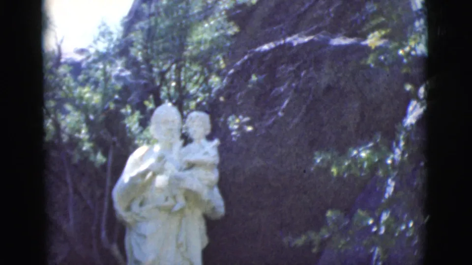 A visitor-shot 1966 Clarkdale, Arizona frame centers a pale mother-and-child style statue against trees and rock in soft focus.