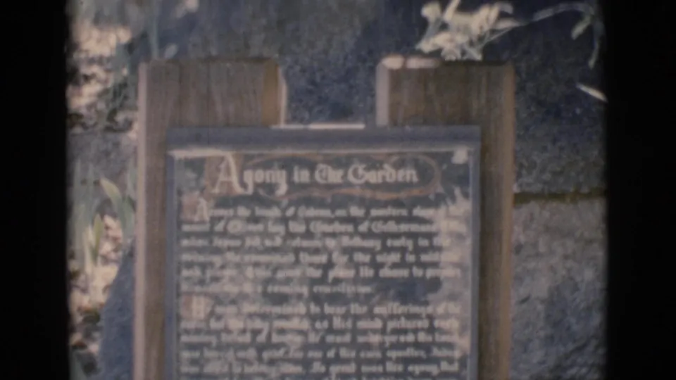 Soft 8mm view of the Agony in the Garden plaque at the Clarkdale, Arizona religious site, with plants and masonry behind it.