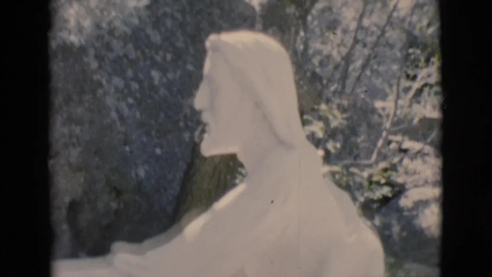 1966 Clarkdale, Arizona frame showing a white robed religious statue, likely Jesus, set outdoors near trees and rocky surroundings.