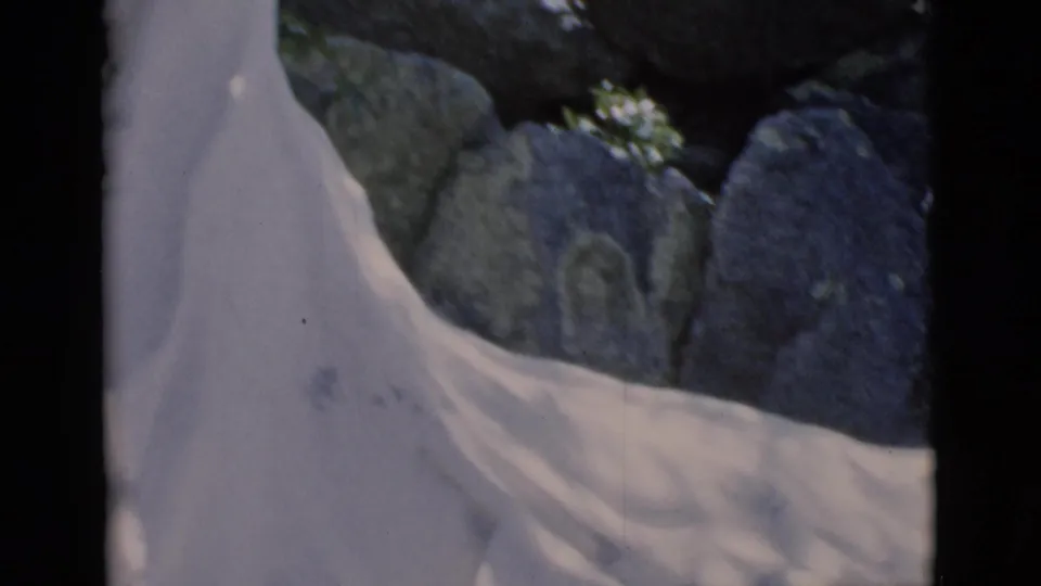 1966 Clarkdale, Arizona 8mm frame showing part of a white religious statue set against rocks and foliage.