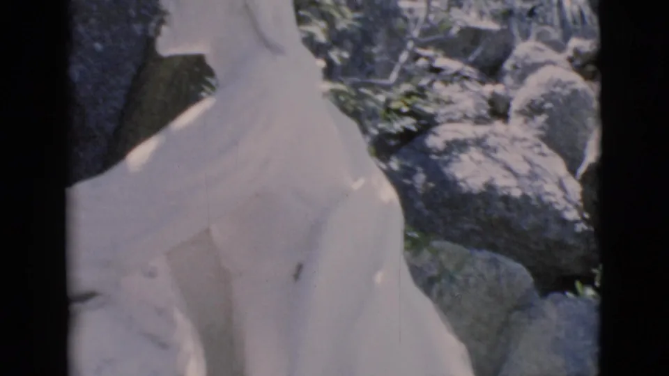 1966 Clarkdale, Arizona frame showing the upper draped form of a white religious statue in a rocky outdoor setting.