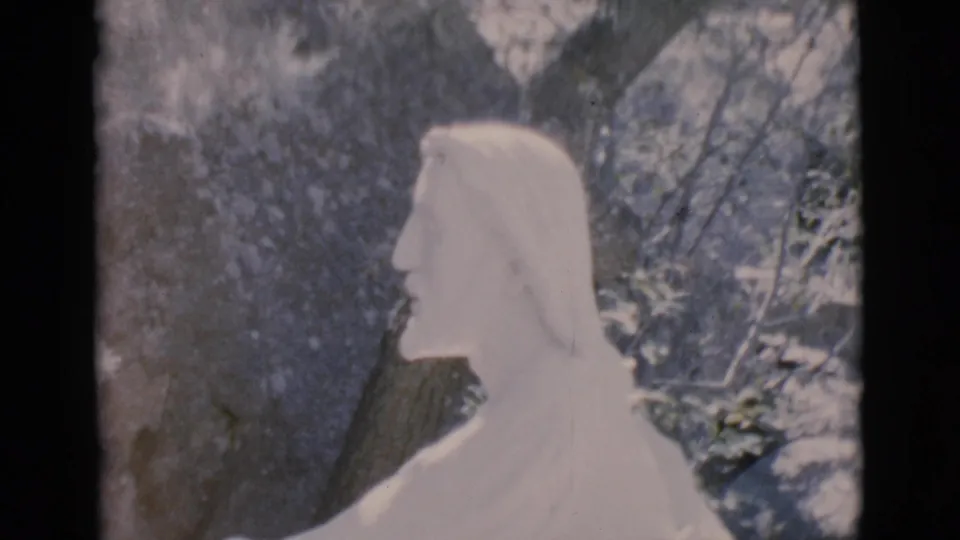 1966 Clarkdale, Arizona frame showing a white robed religious statue in profile amid rocks and foliage on 8mm film.