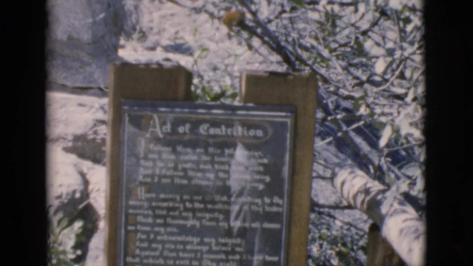 Soft 8mm frame from Clarkdale, Arizona in 1966 showing the Act of Contrition plaque on a wooden sign outdoors.