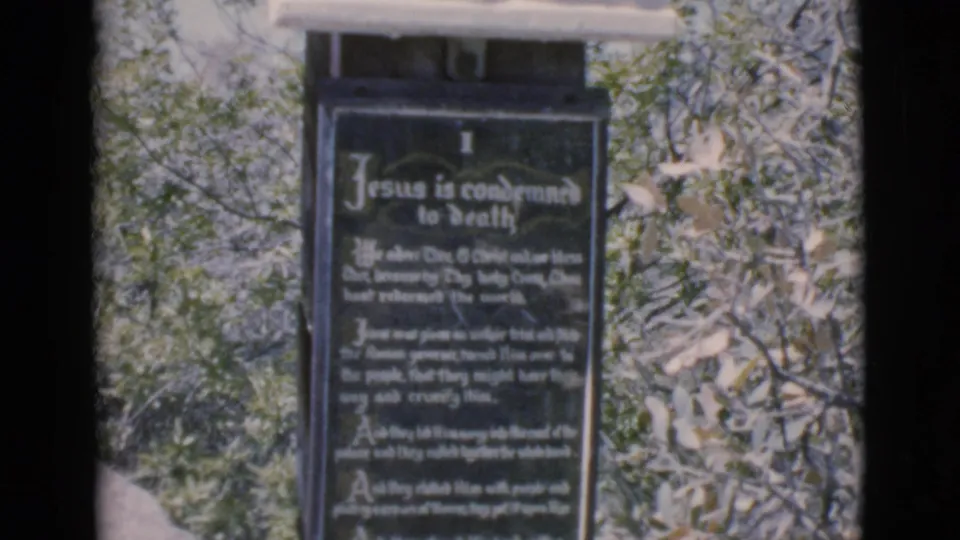 Clarkdale, Arizona home-movie frame of a dark plaque for the Jesus condemned to death station, softened by 8mm focus and grain.
