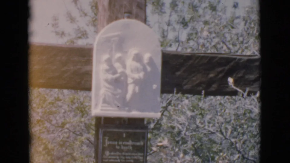 Final 1966 Clarkdale frame shows the wooden cross, pale carved memorial plaque, and dark lower sign surrounded by brush and trees.