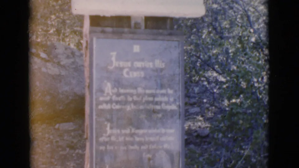 A softly focused 8mm frame of the Clarkdale religious marker, with the Jesus carries His Cross inscription partly legible in sunlight.