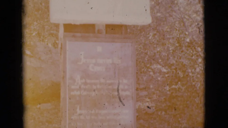 Warm, faded 8mm view of the Clarkdale outdoor religious marker, with the inscription softened by exposure and film wear.