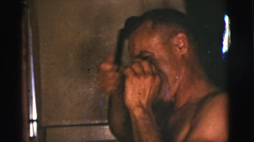 In metadata-supported 1966 Tuscon, Arizona footage, a shirtless man combs his hair in a dim private bathroom.