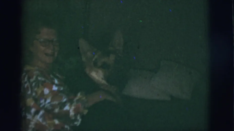 1966 Tuscon, Arizona home-movie frame showing a woman with glasses on a sofa as a German Shepherd leans in beside her.