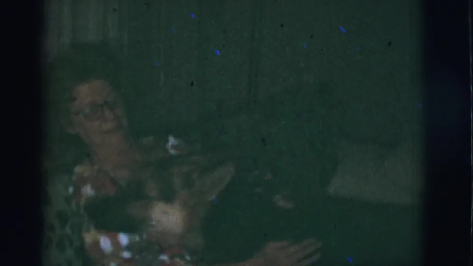 1966 Tuscon, Arizona home-movie frame with a smiling woman on a sofa and a German Shepherd close at her side.