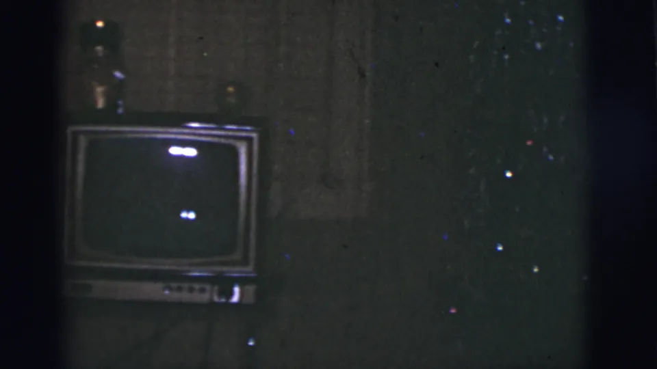 Dim 1966 Tucson living-room frame centered on a boxy television set with walls and reflective film specks visible.