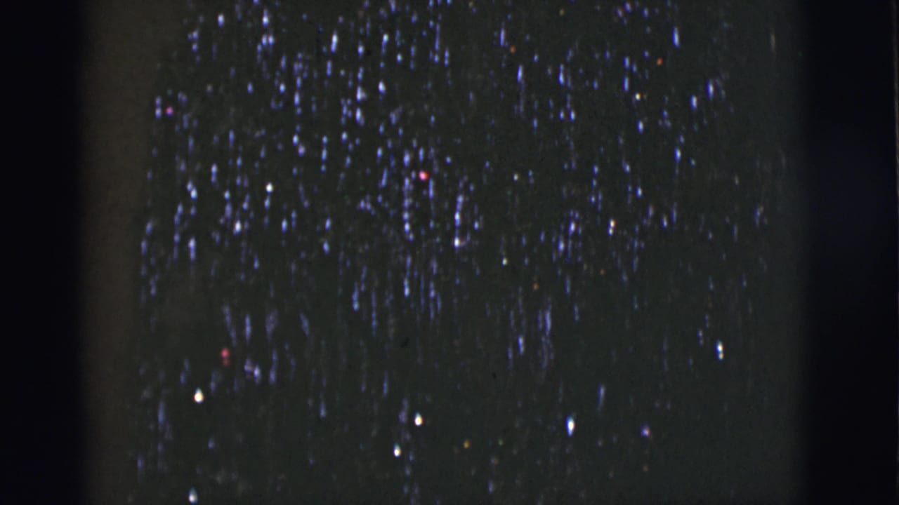 Dark night sky with scattered bright points and blue-purple streaking near soft black film edges.