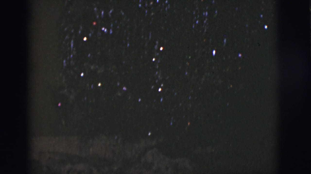 1966 Tuscon, Arizona 8mm frame with sparse night-sky lights, faint blue and red color points, heavy grain, and low-light exposure.