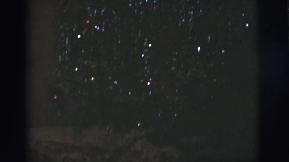 1966 Tuscon, Arizona 8mm frame with sparse night-sky lights, faint blue and red color points, heavy grain, and low-light exposure.