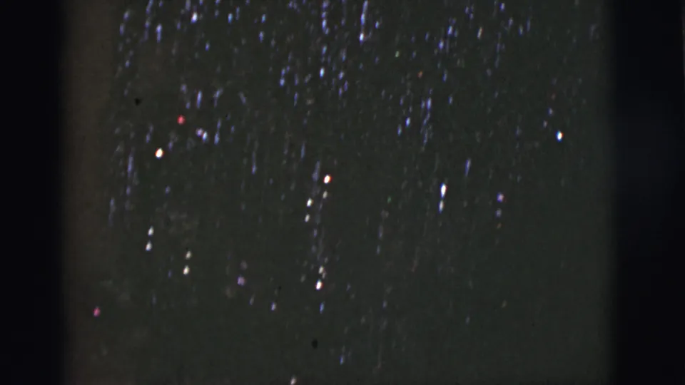 1966 8mm night-sky frame from Tuscon, Arizona with clustered light points, blue-purple streaking, dust, scratches, and soft exposure.