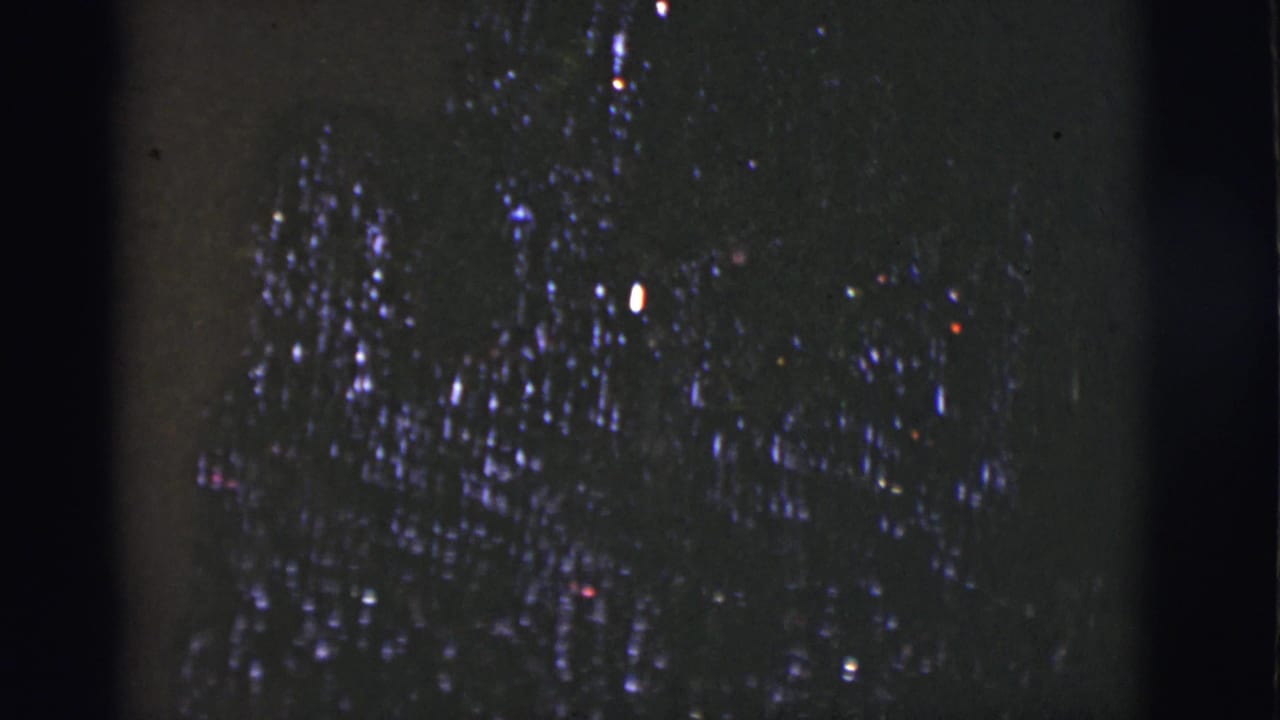 Dark, grainy frame with scattered light specks and little discernible subject detail.
