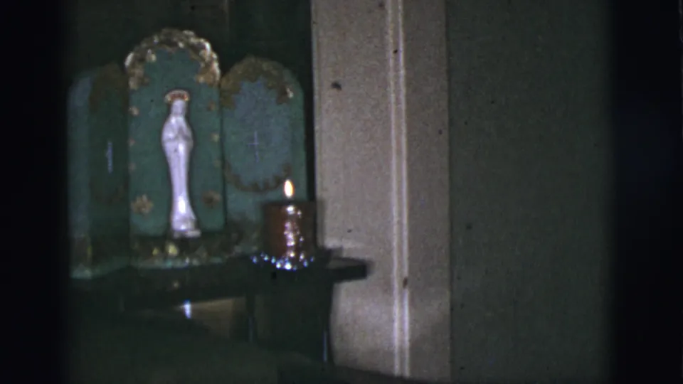 A 1966 Tucson home-movie frame centers a white Virgin Mary statue in an ornate green shrine with a lit candle on a shelf.