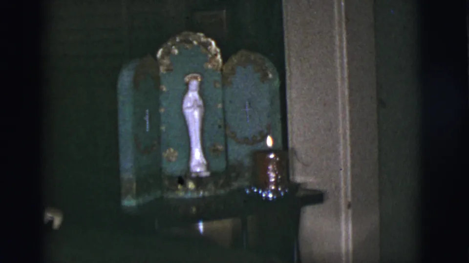 The frame shows a white Virgin Mary statue in a green and gold household shrine with a lit candle, filmed in a dark 1966 Tucson interior.