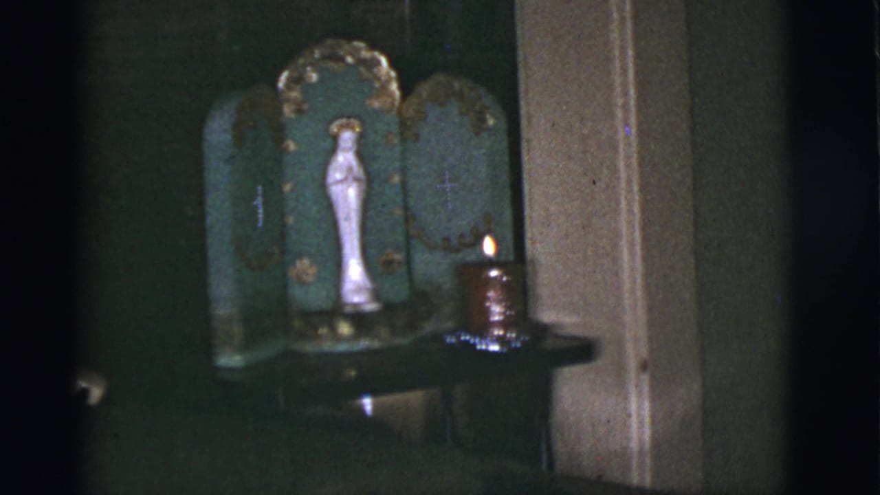 White Virgin Mary statue in a green devotional shrine with a candle burning at the side, filmed indoors in 1966 Tuscon.