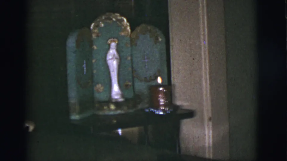 White Virgin Mary statue in a green devotional shrine with a candle burning at the side, filmed indoors in 1966 Tuscon.