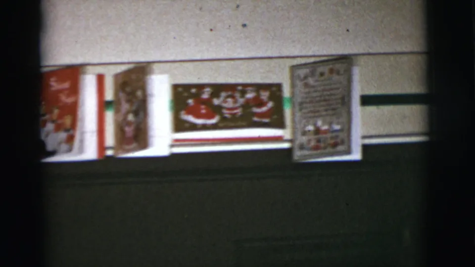 1966 Tucson-area 8mm frame showing several Christmas cards, including Santa-themed artwork, mounted above a dark lower wall or panel.