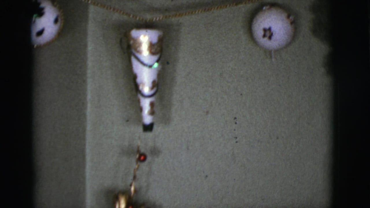 Close 1966 home-movie view of a white cone decoration and round star-marked ornament on an interior wall.