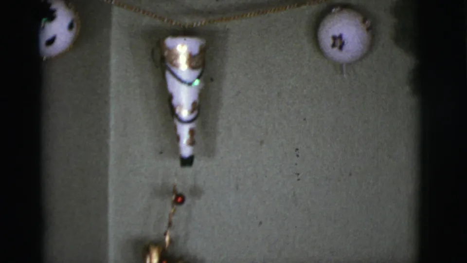 Close 1966 home-movie view of a white cone decoration and round star-marked ornament on an interior wall.
